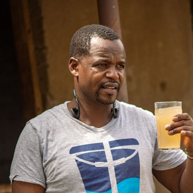 Man holding a glass of murky water while wearing a gray Bucket Ministry shirt